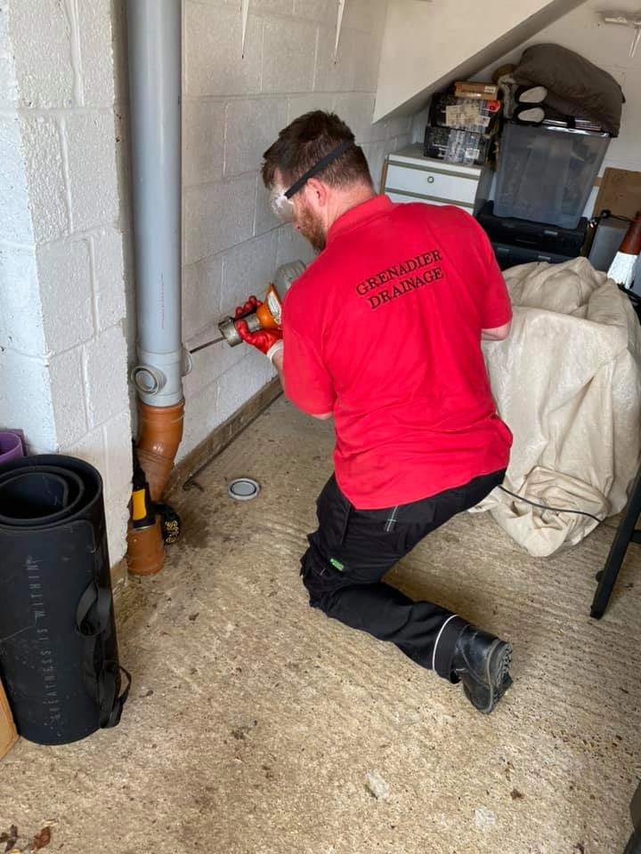 photo-54 Grenadier Drainage technician using professional equipment to service internal waste pipes, wearing safety goggles and red company uniform.